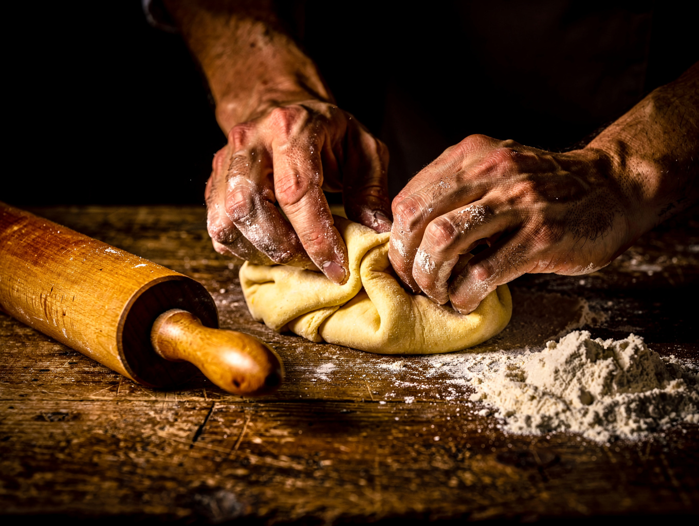 Chef hand-rolling fresh pasta in a warm, candlelit kitchen